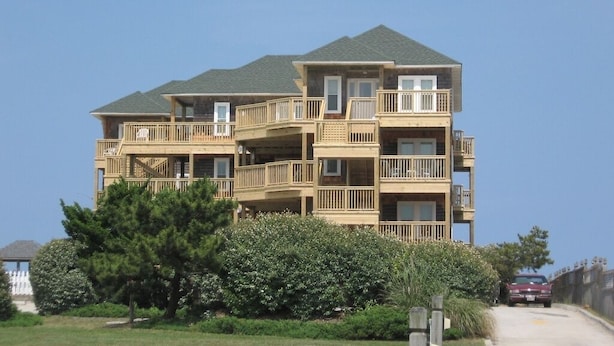A multi-story residential building with balconies, a wooden facade, and a clear sky.