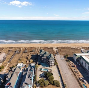 Vista aerea di una zona costiera con spiaggia, piscina e numerosi edifici.