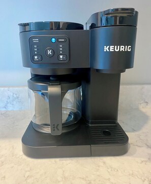 A Keurig coffee maker with a clear carafe and a black base, featuring a digital control panel with various settings.