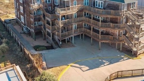 A multi-story building with balconies, a pool, and a beach view.