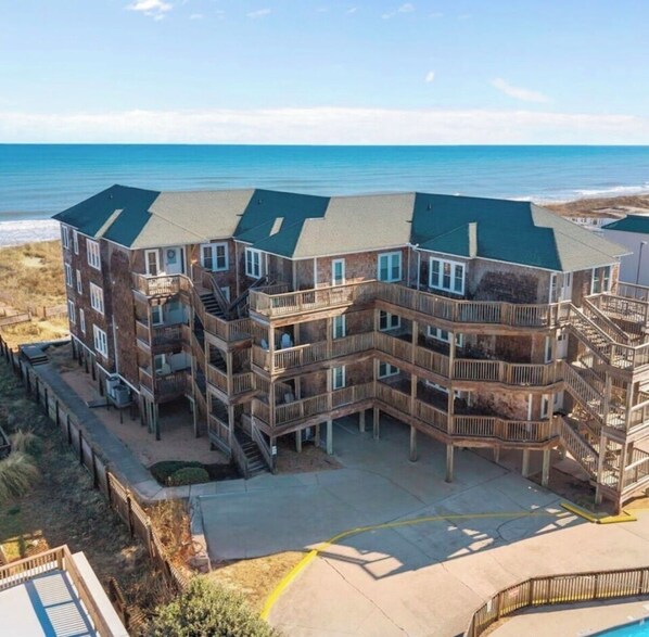 A multi-story building with balconies, a pool, and a beach view.