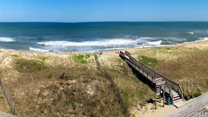 A beach with a wooden boardwalk leading to a small structure, likely a restroom or shelter, near the water's edge.