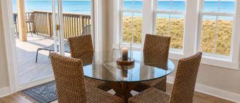 Une table ronde en verre, quatre chaises en osier, une bougie et une vue sur la plage à travers de grandes fenêtres.