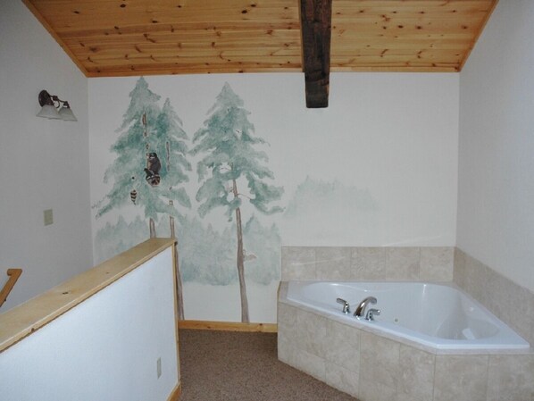 A bathroom with a bathtub, wooden ceiling, and a wall with a tree mural. - Convenient location! Downtown Loft at the River Confluence, Walk to Restaurants (Estes Park)