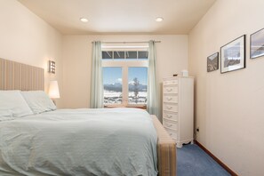 A bedroom with a bed, a dresser, a window with a view of snow-covered mountains, and a lamp.