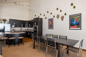 A modern kitchen with dark cabinets, a central island with stools, and a dining area with a long table and chairs. - Spectacular Modern Lodge with on-site Concierge!  Amazing Views! (Fraser)