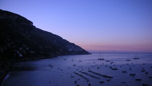 Eine Küstenlandschaft mit zahlreichen Booten, die in ruhigem Wasser vor Anker liegen, einer felsigen Küste und einem klaren Himmel.