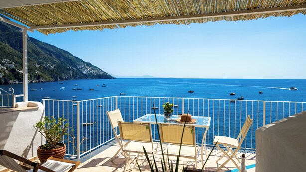 Ein Balkon mit Tisch und Stühlen mit Blick auf ein Meer und Boote.