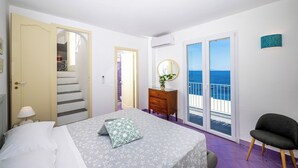 Ein Schlafzimmer mit Bett, Kommode, Stuhl und Meerblick durch eine Schiebetür.