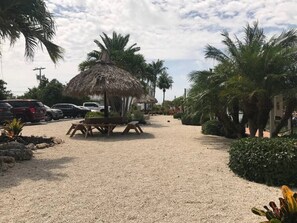 A parking area with cars, a thatched-roof structure, and palm trees. - Dbl Master |Oceanview |Jacuzzi |Beach |Marina |BBQ (Tavernier)