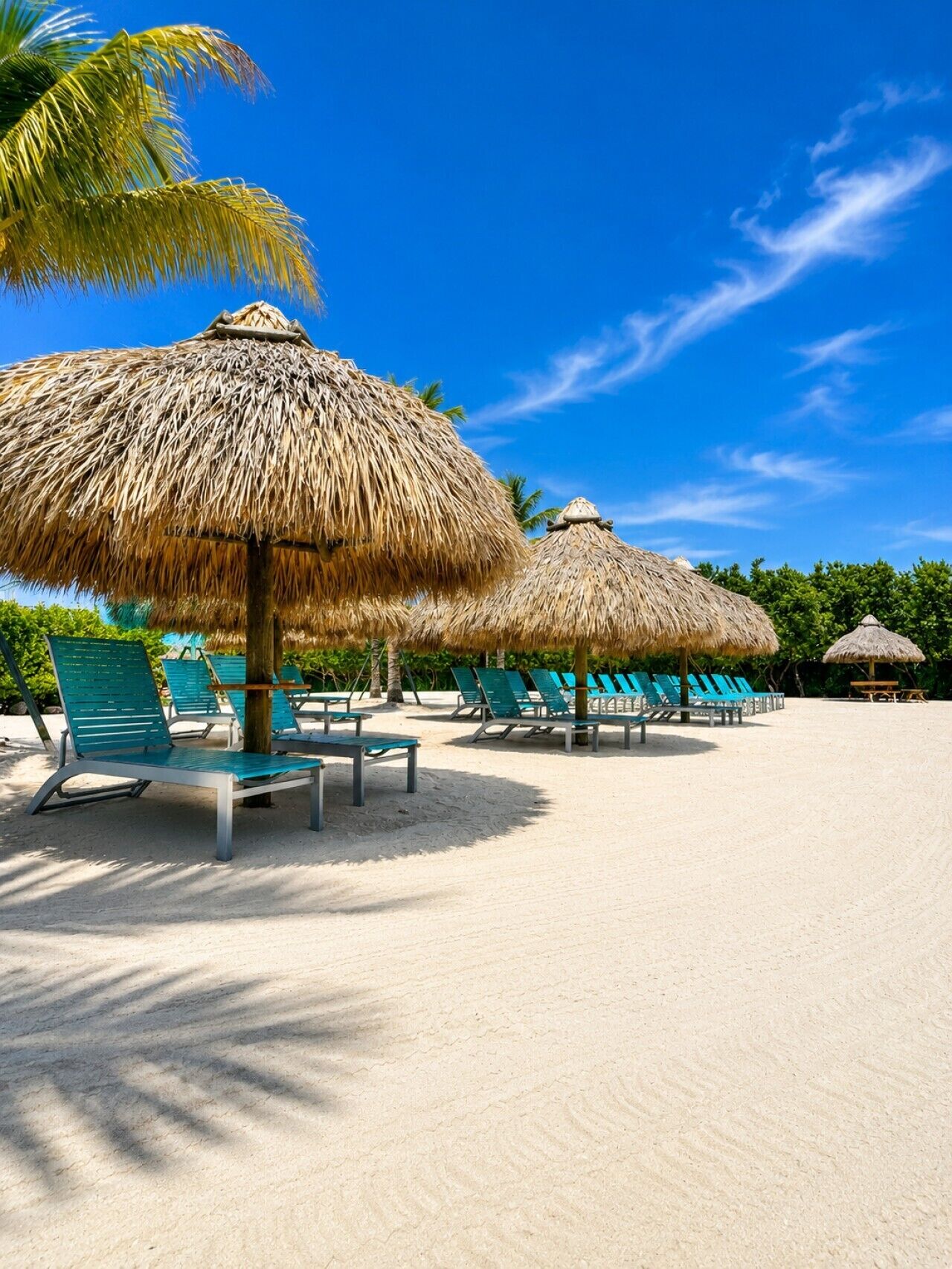 A beach with thatched umbrellas and green lounge chairs.