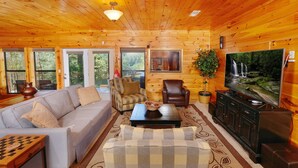 Ein gemütliches Holzhaus-Interieur mit einer Couch, einem Sessel, einem Fernseher und einem Schachtisch.