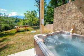 Ein Whirlpool mit Steinsandsteinwand, ein Picknicktisch und eine Rasenfläche mit Bäumen und Bergen im Hintergrund.
