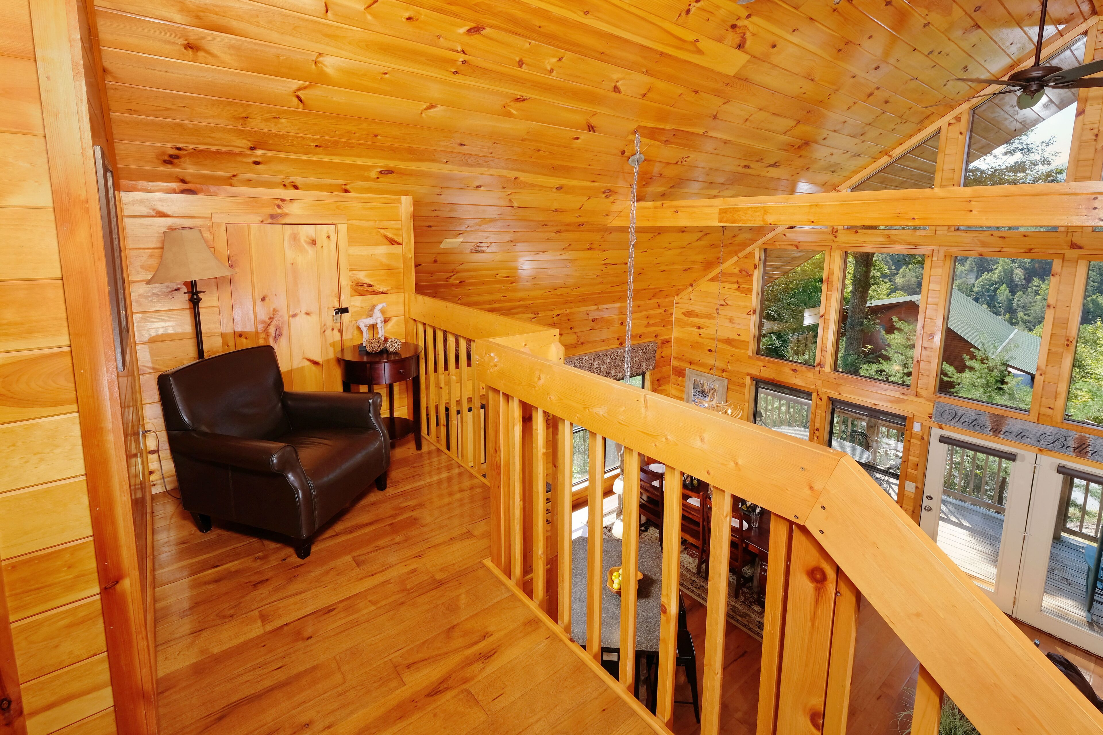 A wooden cabin interior with a wooden staircase, a leather sofa, and a view of the surrounding forest.