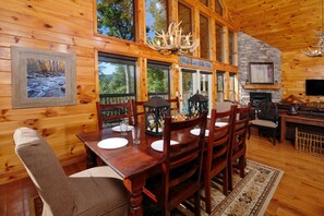 Ein Interieur einer Holzhütte mit einem Esstisch, gedeckt für vier Personen, einem Kamin und einem Schild mit der Aufschrift 'Welcome to Bella Vista'.