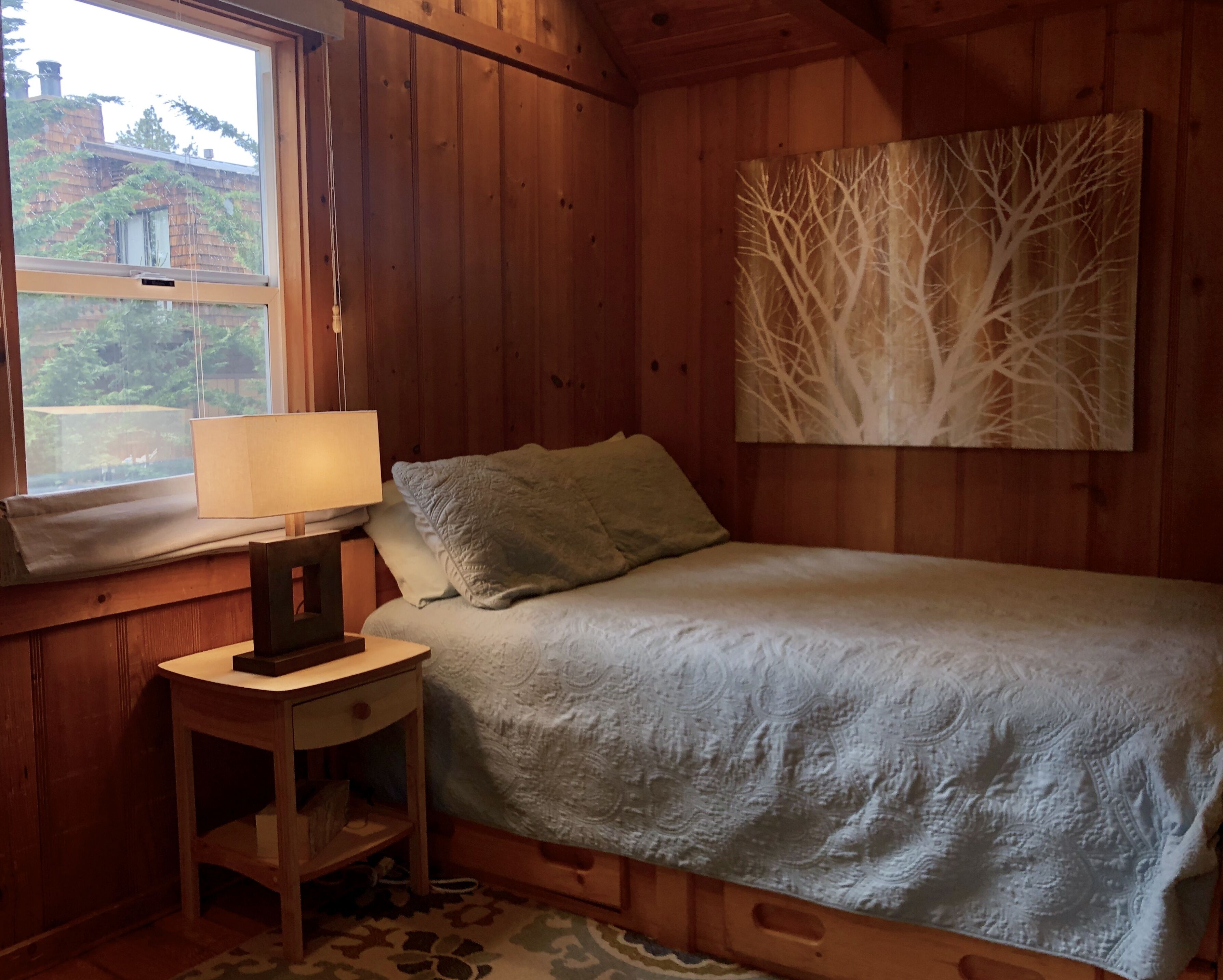 Une chambre confortable dans un chalet, avec un lit, une table de chevet avec une lampe, une fenêtre et un tableau au mur.