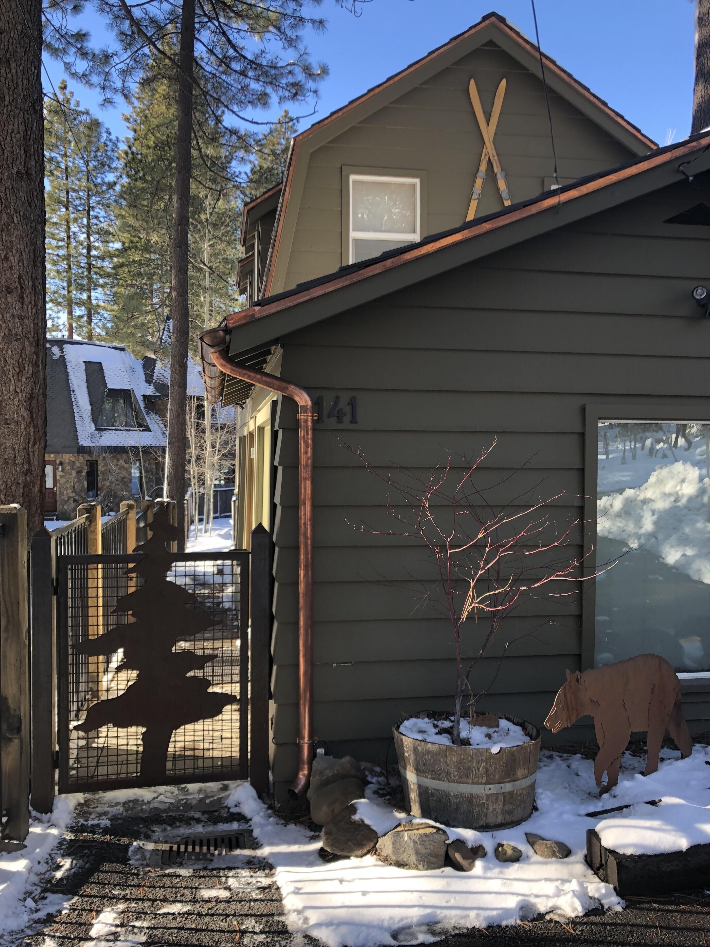 A house with a number 141, a wooden fence, a snow-covered ground, and a tree in the foreground.