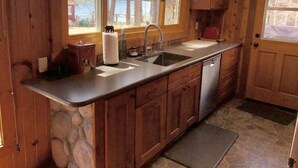 Une cuisine rustique aménagée dans une cabane en bois, avec un mur en pierre, un évier, une cuisinière et une fenêtre donnant sur un lac.