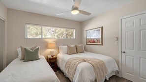 A bedroom with two beds, a ceiling fan, a window with blinds, a bedside table with a lamp, and a door. - Private Paradise: Chef’s Kitchen and Acre Escape (Scottsdale)
