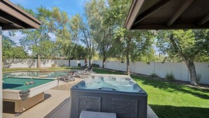 Patio trasero con piscina, jacuzzi y sillas de descanso.