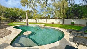 Una piscina con cubierta de piedra, rodeada por un césped y una pared blanca.