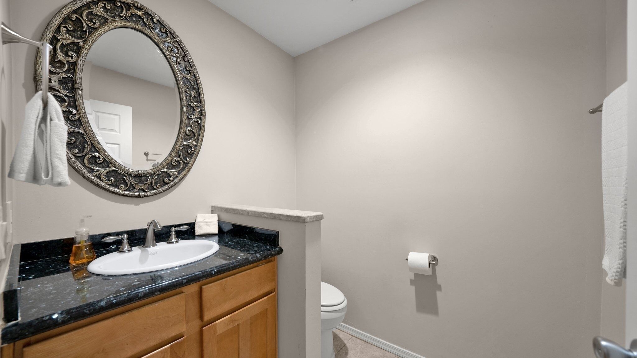 A bathroom with a round mirror, a sink, a toilet, and a towel rack.