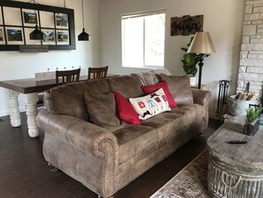 A cozy living room with a brown leather sofa, a wooden dining table, and a stone fireplace.