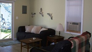 A living room with a sofa, a coffee table, a lamp, and a window with blinds. - Sand Lake Cottage - near Tawas (National City)