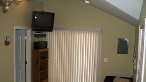 A living room with a television, a bookshelf, a sofa, and a window with blinds. - Sand Lake Cottage - near Tawas (National City)