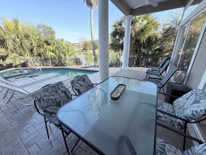 A glass-top table with chairs, a pool, and palm trees in the background.