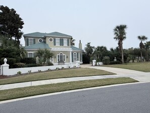 A two-story house with a green roof, a front porch, and a well-maintained lawn.