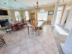 A spacious dining area with a large wooden table and chairs, a fireplace, and a view of the outdoors through large windows.