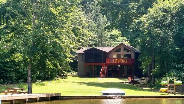 A lodge with a large glass facade, a red staircase, and a dock extending into a lake, surrounded by dense trees. - Amazing Waterfront Home in Private setting w/ fiber internet! (Bumpass)