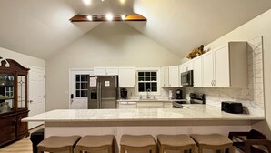 A modern kitchen with white cabinets, a stainless steel refrigerator, a microwave, and a large island with bar stools. - Amazing Waterfront Home in Private setting w/ fiber internet! (Bumpass)