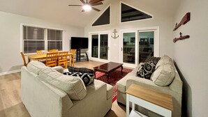 A living room with a sofa, a coffee table, a TV, and a dining area with a table and chairs. - Amazing Waterfront Home in Private setting w/ fiber internet! (Bumpass)