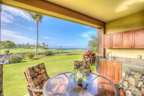A room with a glass table, chairs, and a view of a golf course and ocean.