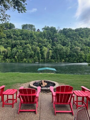 Vista al lago con un pozo de fuego y sillas Adirondack rojas.