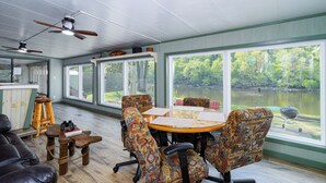 Uma área de refeições com mesa e cadeiras, um bar e amplas janelas com vista para um lago.
