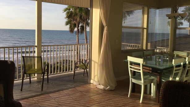 A balcony with a view of the ocean, a glass table, chairs, and a railing.