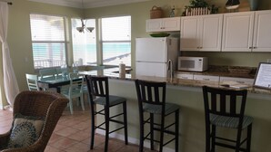 A kitchen with a dining area, featuring a refrigerator, microwave, and a window with blinds.