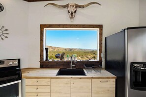 A kitchen with a wooden countertop, a black sink, a stainless steel refrigerator, and a window with a view of a desert landscape. - Crystal Valley Cabin: Modern-Rustic Style&Comfort (Alpine)