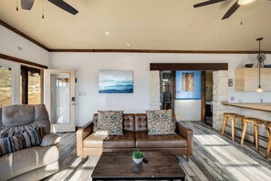 A living room with a brown leather sofa, a coffee table with a plant, and a wooden bar area with stools. - Crystal Valley Cabin: Modern-Rustic Style&Comfort (Alpine)