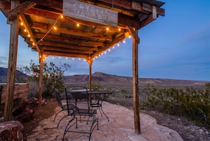 A wooden pergola with string lights, a table, and chairs in a desert landscape. - Crystal Valley Cabin: Modern-Rustic Style&Comfort (Alpine)