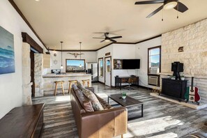 A spacious living area with a stone wall, a fireplace, a television, and a guitar. - Crystal Valley Cabin: Modern-Rustic Style&Comfort (Alpine)