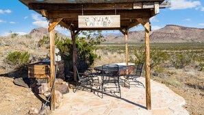 A wooden gazebo with a sign reading "Crystal Valley," surrounded by a stone patio with metal chairs and a table.