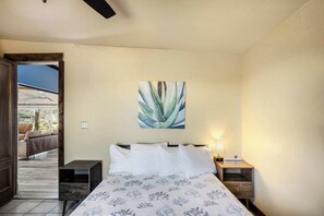 A bedroom with a bed, a nightstand, a wall-mounted painting, and a view of an outdoor seating area. - Crystal Valley Cabin: Modern-Rustic Style&Comfort (Alpine)