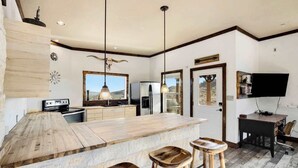 A modern kitchen with a large island, bar stools, a refrigerator, and a TV mounted on the wall.