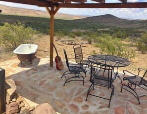 An outdoor patio with a stone floor, a round metal table with chairs, a vintage bathtub, and a guitar leaning against a wooden post. - Crystal Valley Cabin: Modern-Rustic Style&Comfort (Alpine)