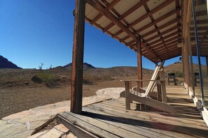 Una terraza de madera con zona cubierta, un sendero de piedra y vistas a un paisaje desértico con montañas al fondo.