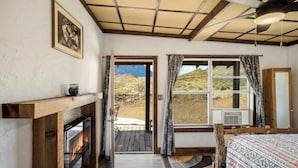 A room with a fireplace, a large window with curtains, a bed, and a door leading outside.